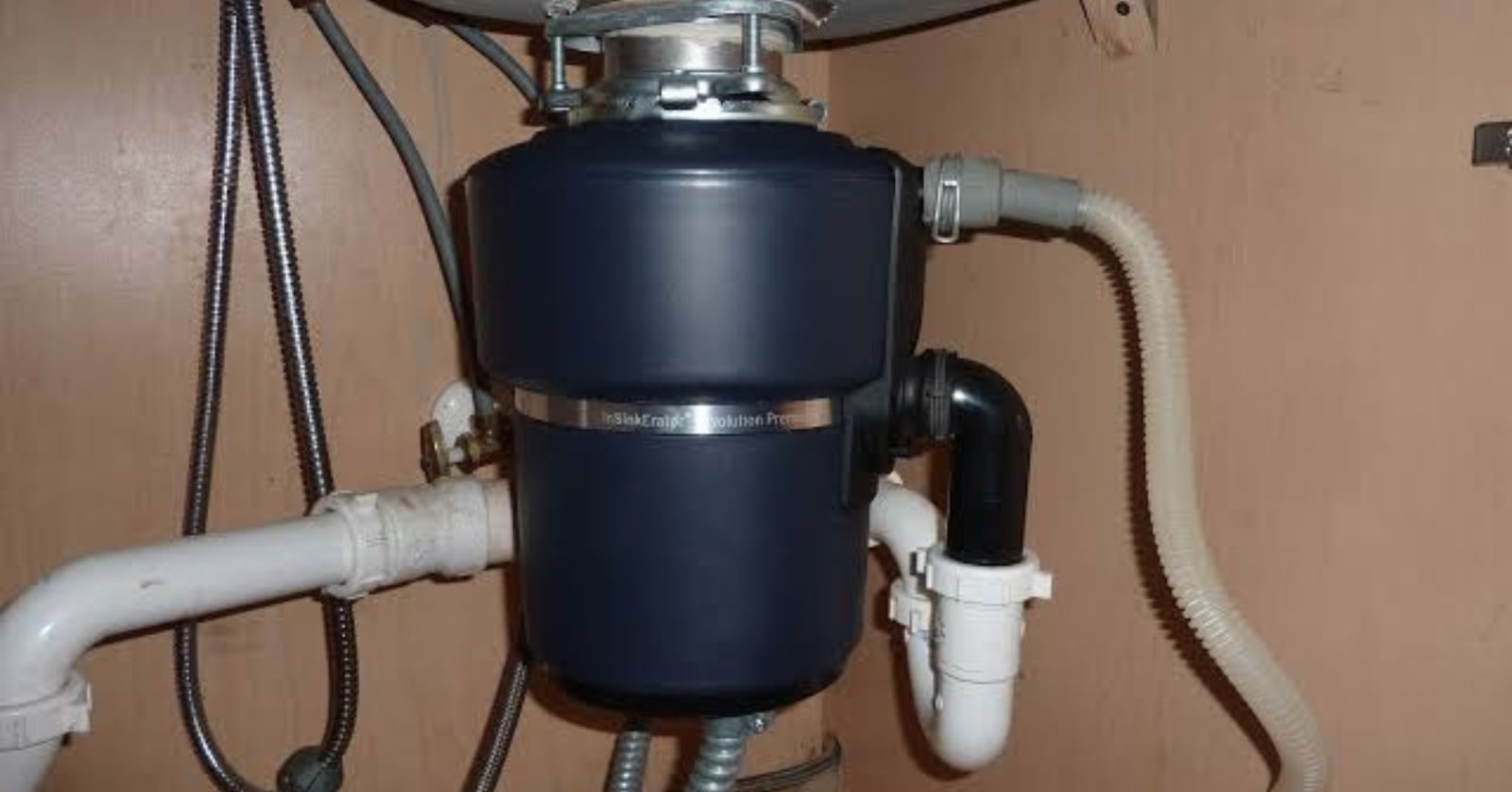 A garbage disposal unit mounted under a kitchen sink with its drain and dishwasher hose attached.