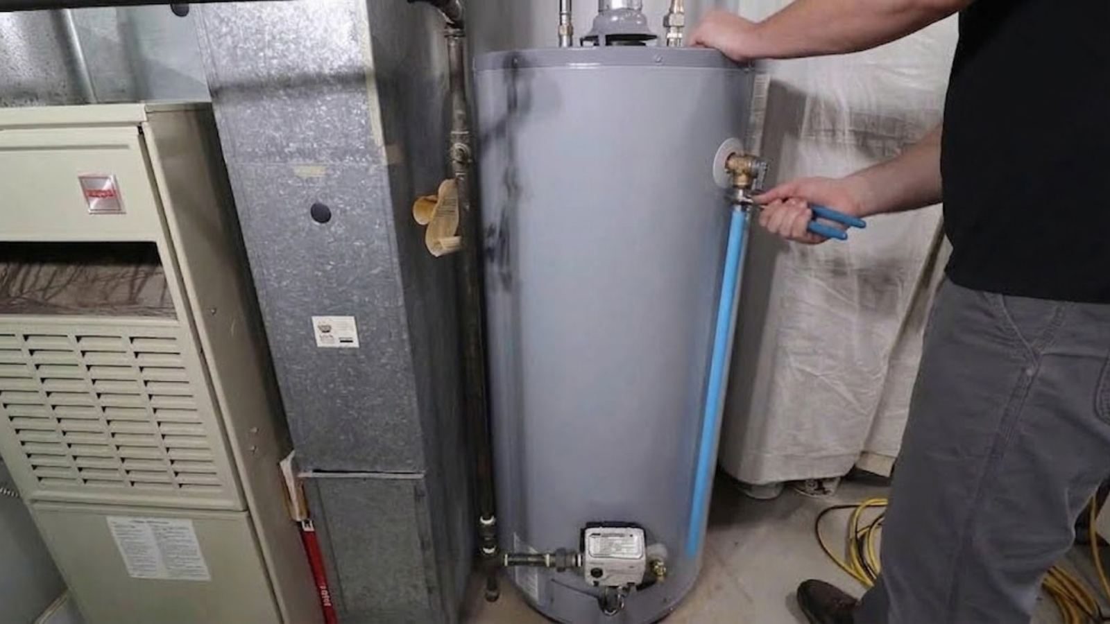 A technician connecting a new tank water heater next to a furnace in a utility area.